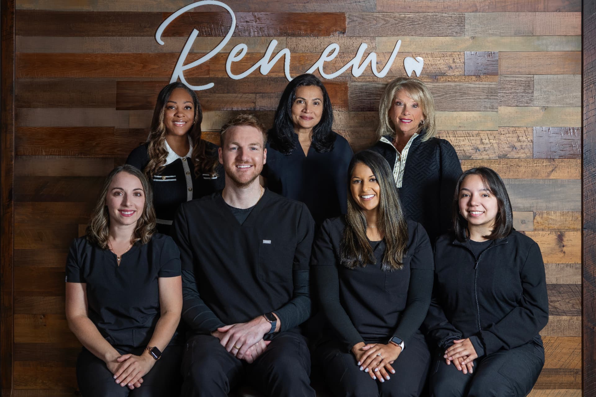 The Renew Dental Loft team in front of the reclaimed-wood wall with the Renew sign