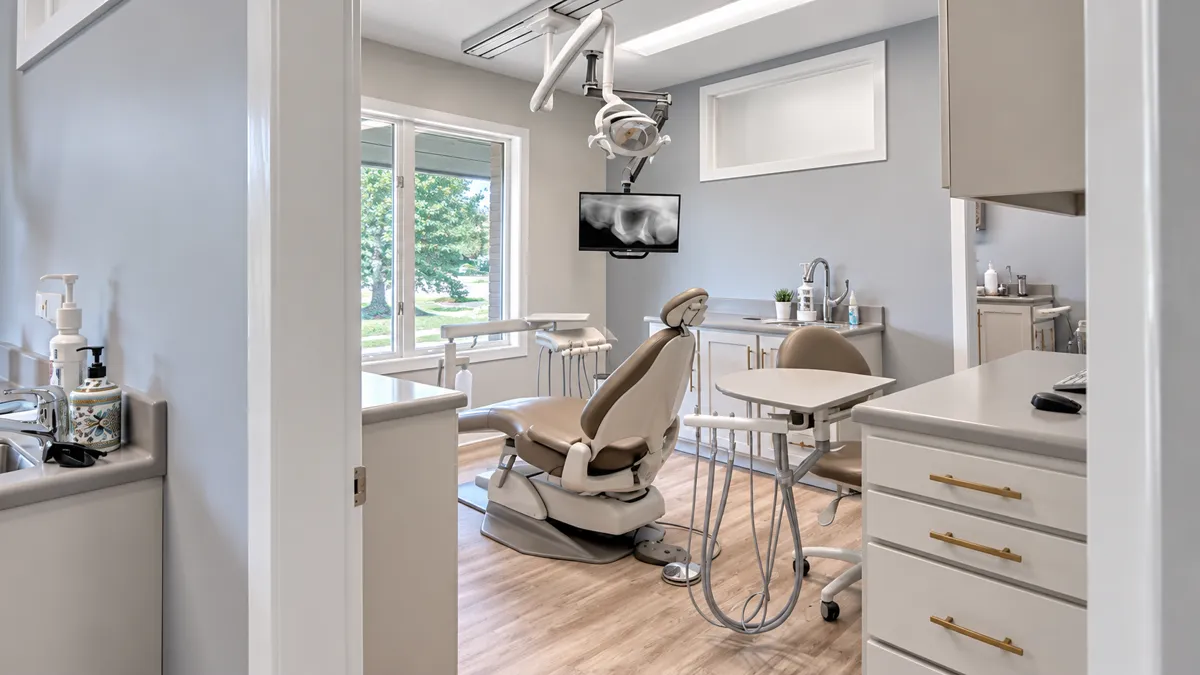 View through a doorway into a calm treatment room with a window, monitor and white cabinets