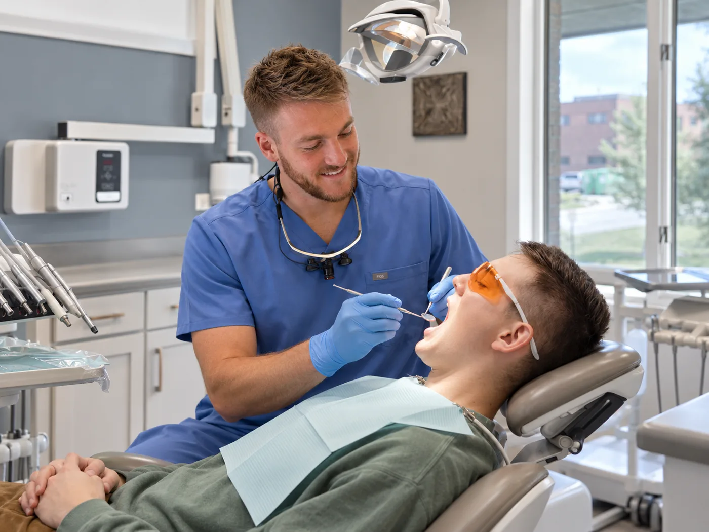 A Renew Dental Loft dentist in blue scrubs smiling while examining a relaxed patient in the treatment chair
